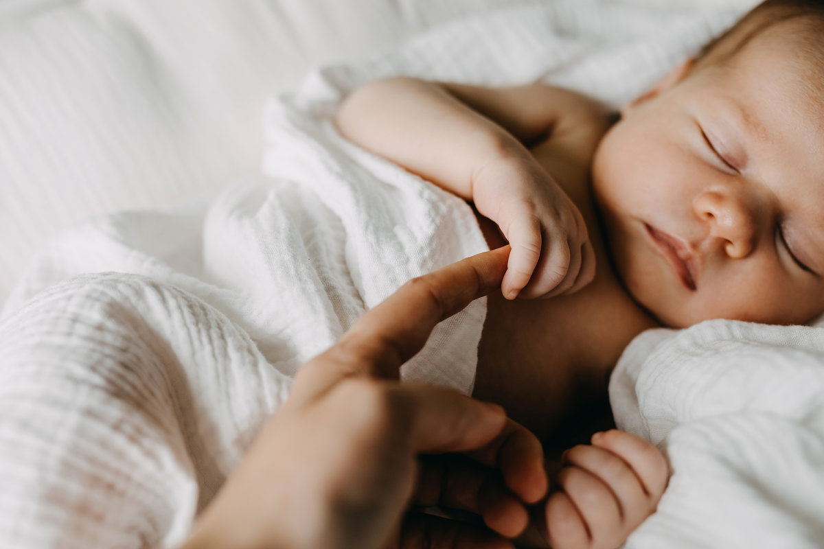 Closeup of a newborn baby holding mother's finger.